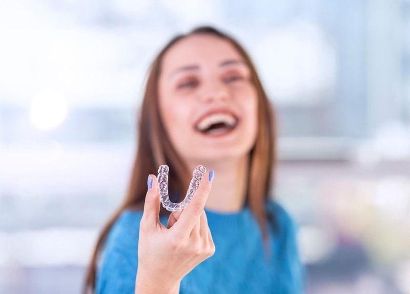 A woman holding a clear aligner.