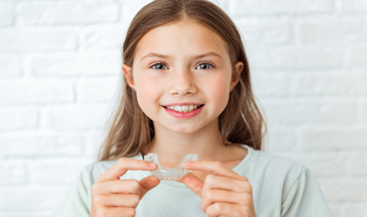 Smiling child girl with perfect and healthy teeth using removable braces or aligner for straightening and whitening teeth. Orthodontic treatment for correction of bite