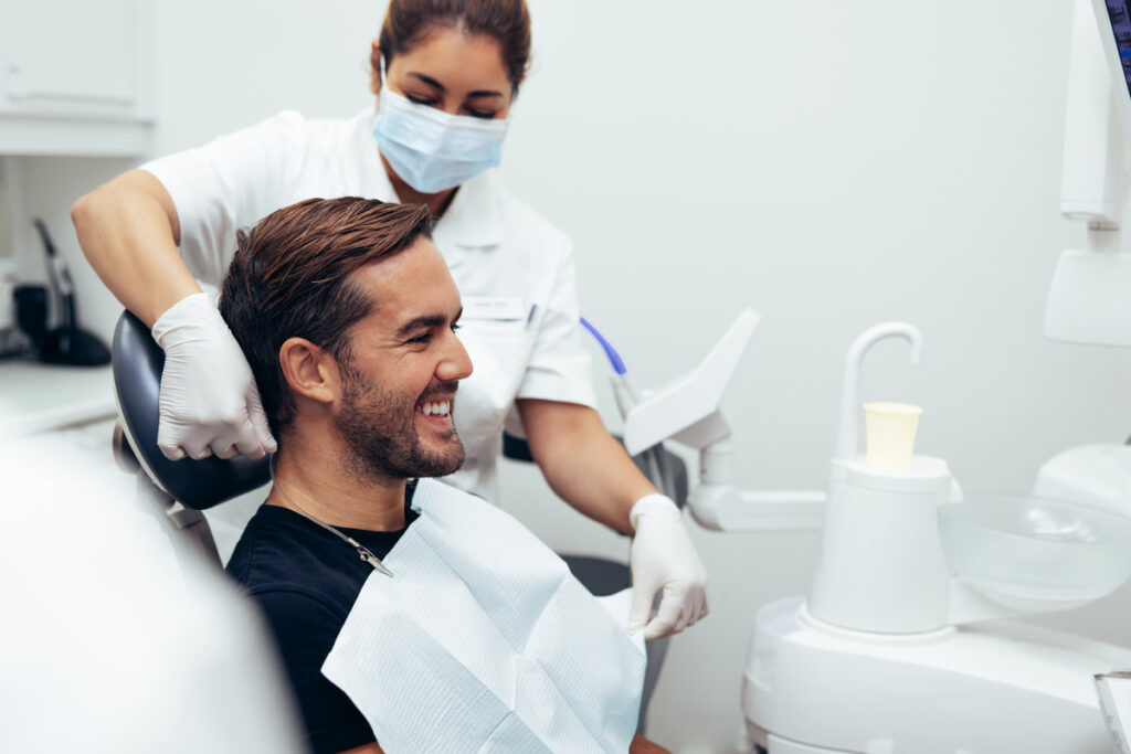 Nurse removing the apron from male patient after dental treatment in a clinic. Male patient smiling after his dental treatment.