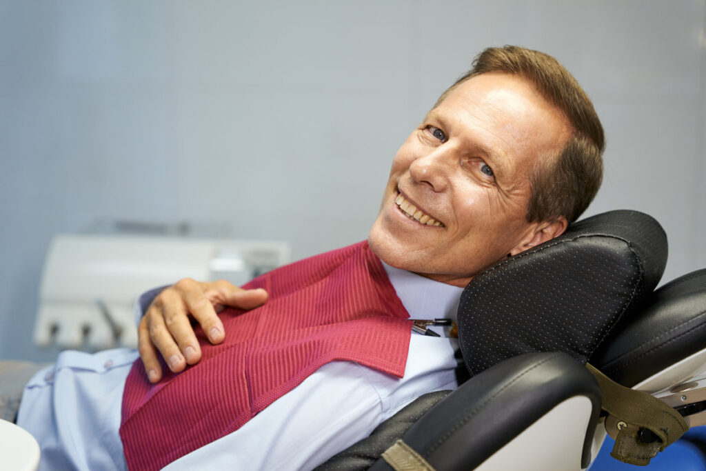 Waist-up photo of an optimistic man smiling while laying down in dental chair